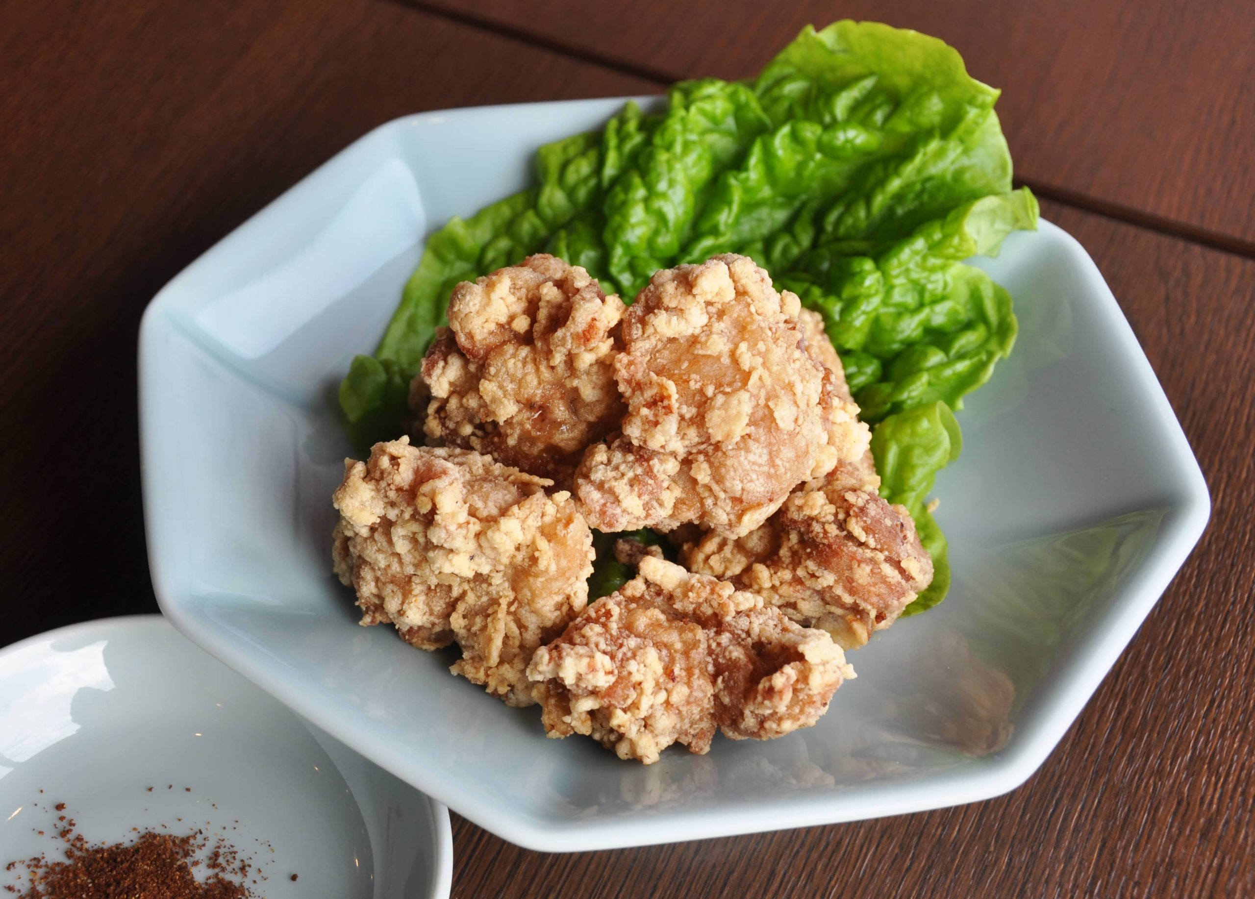 White plate with crispy fried chicken over a green leaf lettuce with a small white plate with spices