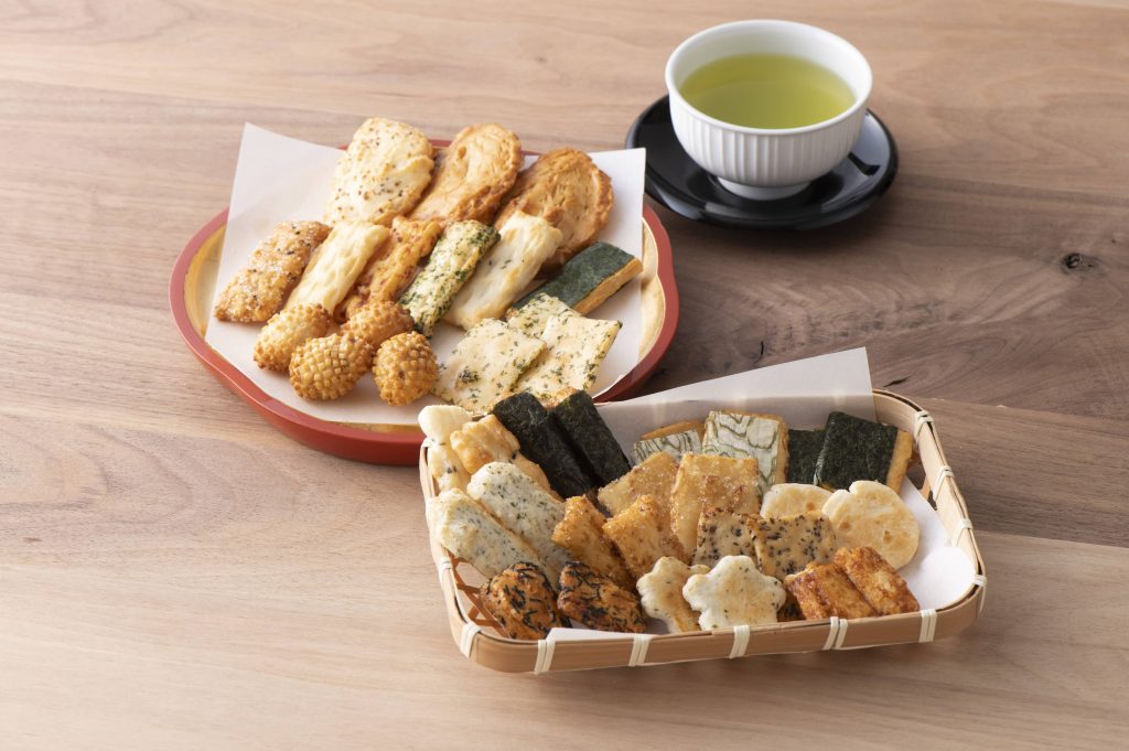 Two dishes filled with an assortment of rice crackers served with a cup of green tea