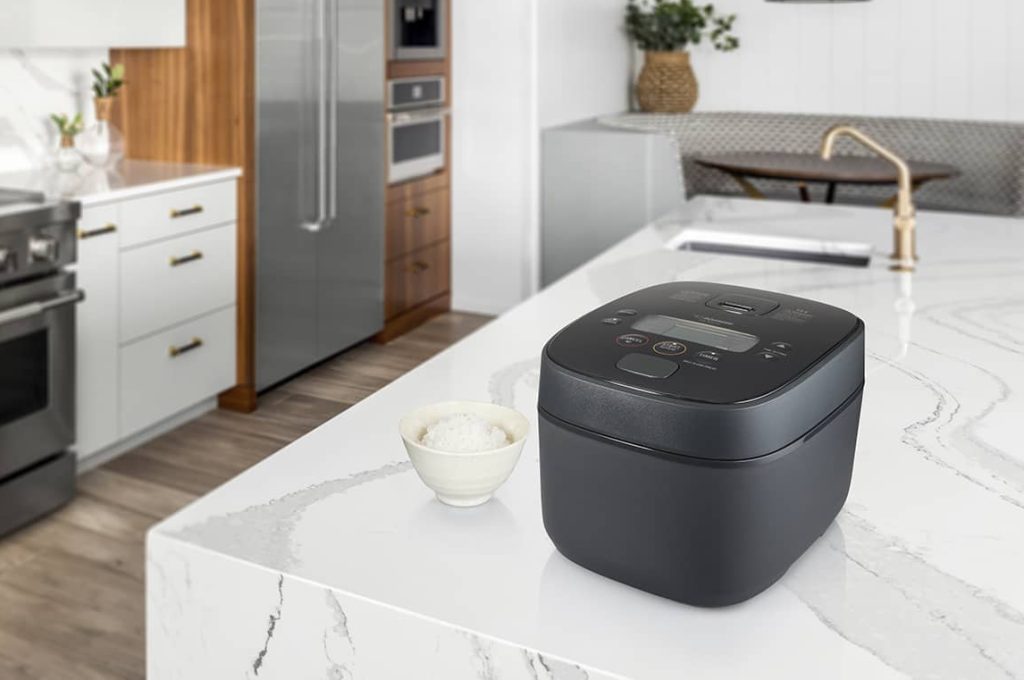 Bright kitchen with white marble countertops with a kitchen island and a modern rice cooker in black in the foreground 