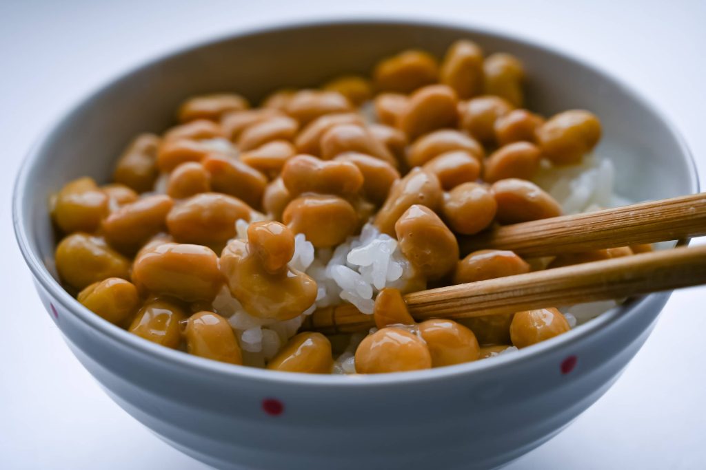 Bowl of rice topped with fermented soy beans and chopsticks taking a portion out