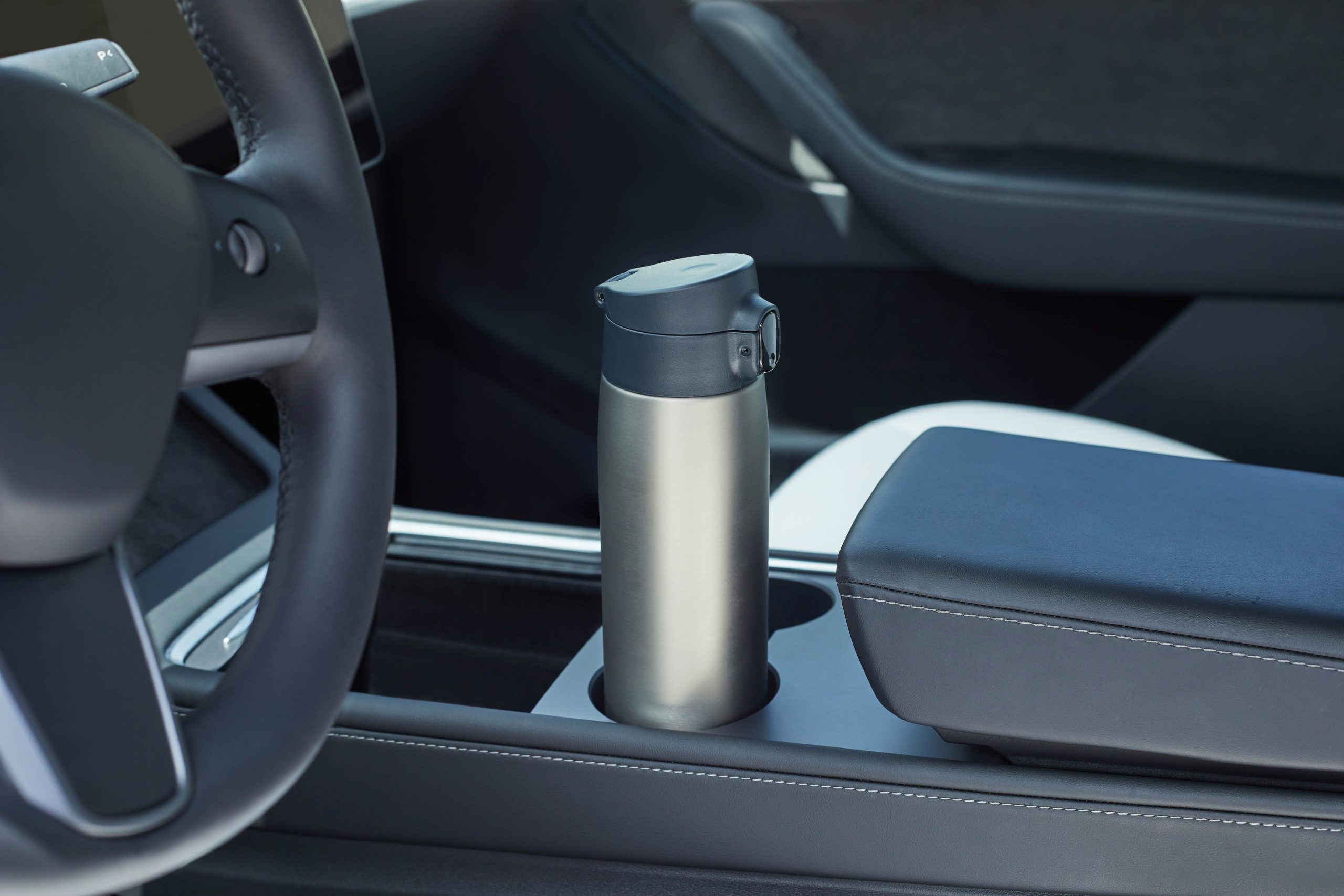 Car interior in dark colors with a stainless steel mug in the cup holder