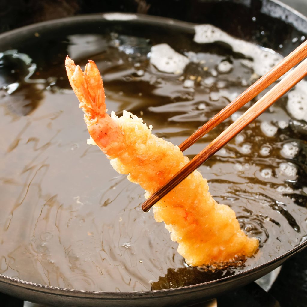 A battered shrimp being taking out of a frying pan filled with hot oil.