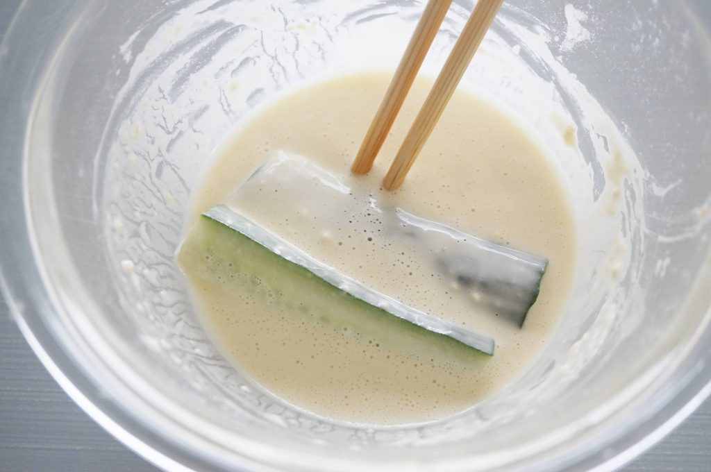 Bowl of tempura batter with a couple of zucchini slices being dipped