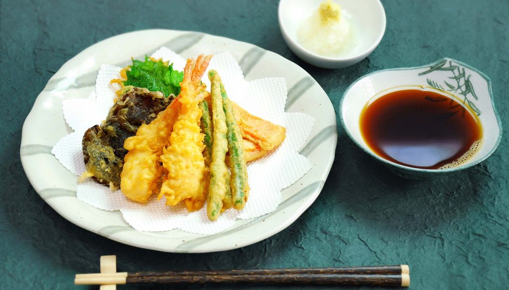 Plate with assorted veggie and shrimp tempura on a green table with a pair of chopsticks in front