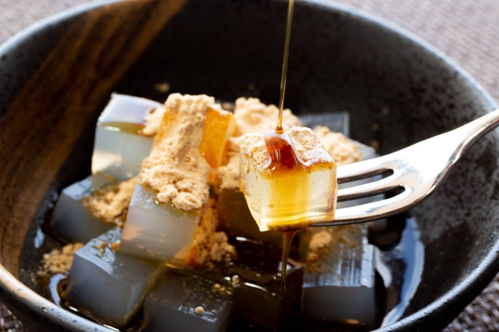 Bowl filled with translucent cubes over sweet sauce and soy bean powder