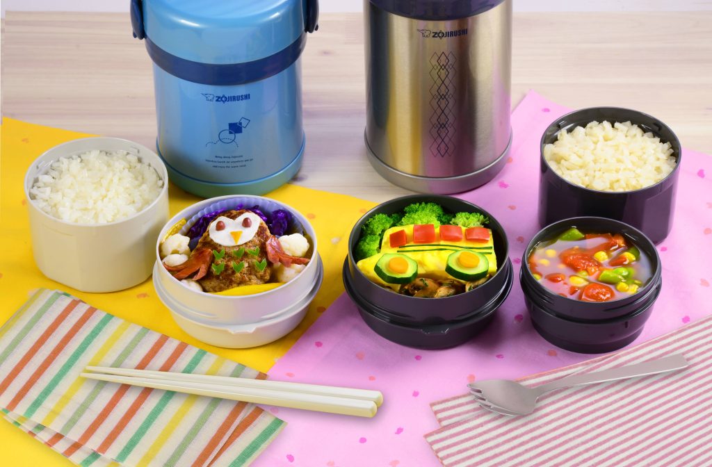 On the left, is a blue lunch jar with a container of rice and a container with a lunch in the shape of an owl. On the right, a gray stainless lunch jar with three containers, one has a lunch in the shape of a school bus, another container with a veggie soup, and riced cauliflower on the largest container