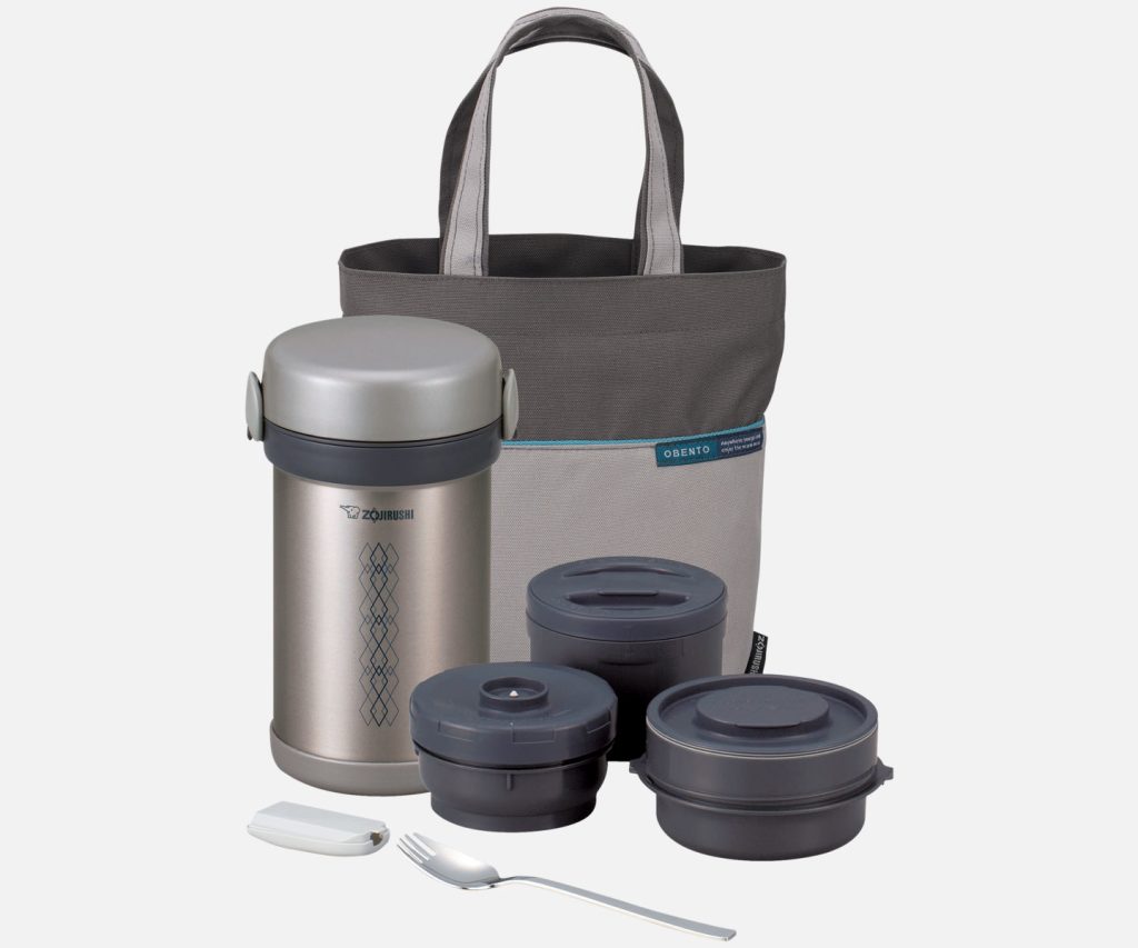 Stainless gray lunch jar with 3 separate containers on the right, a forked spoon with a cover in the front, and a two toned gray carry tote in the back