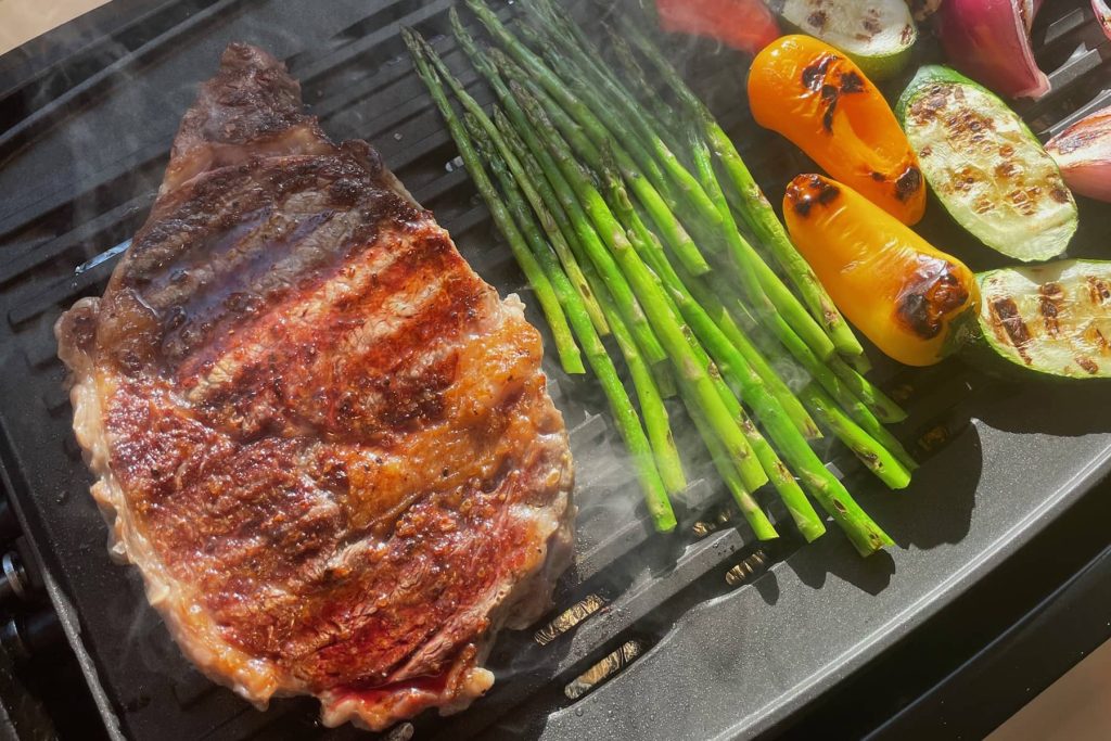 Smoky grilled steak with char lines alongside roasted veggies