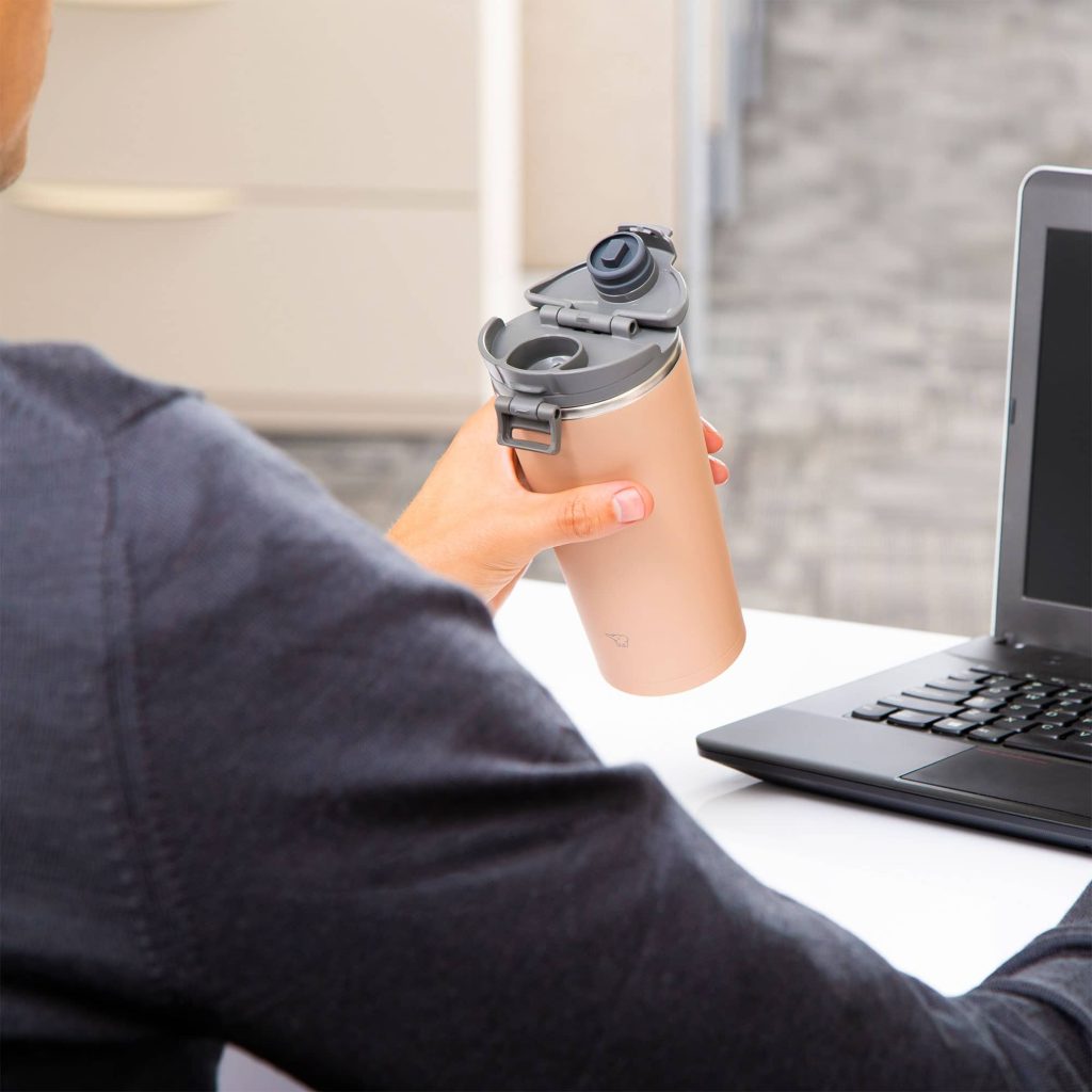 Man sitting on a desk in front of a laptop holding a light cinnamon brown tumbler in his left hand