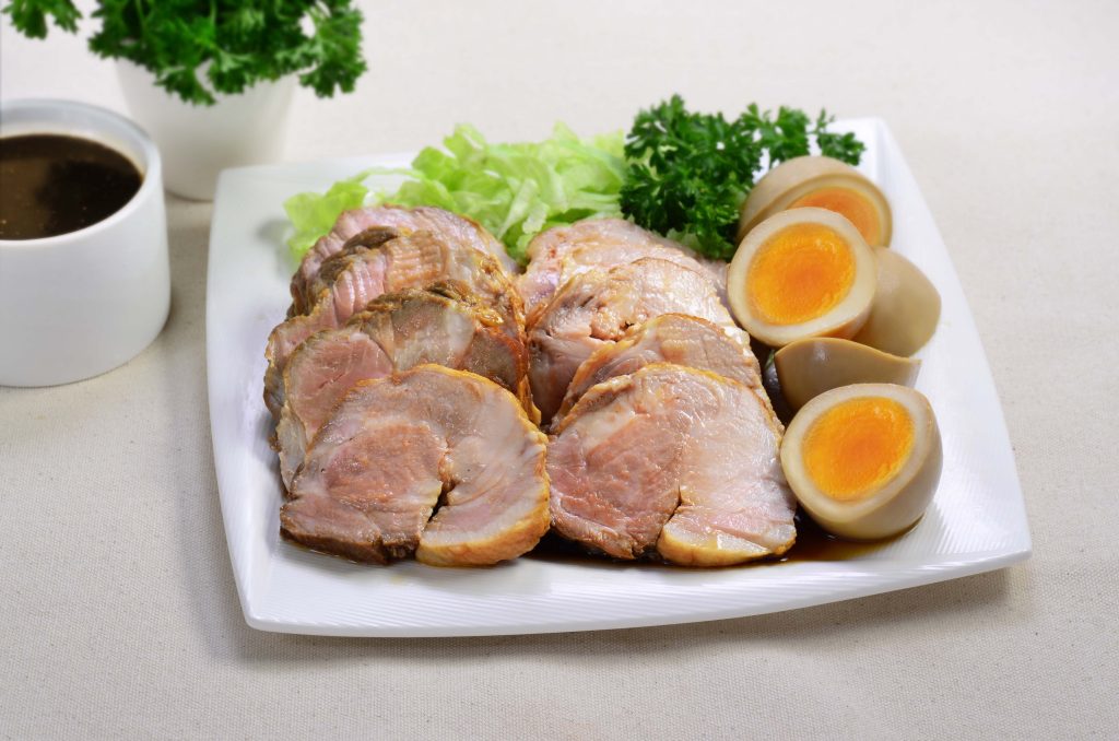 Plate with slices of braised pork and braised eggs cut in half with a side of dipping sauce.