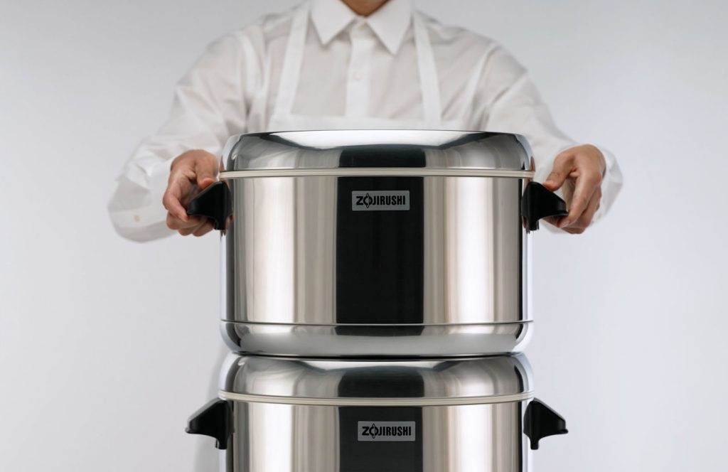 Person holding the rice warmer by the two handles on the side stacking a warmer on top of the other.