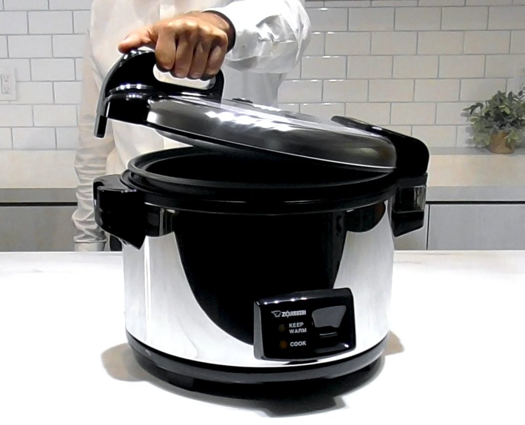 Large stainless rice cooker in a kitchen and someone is opening the lid