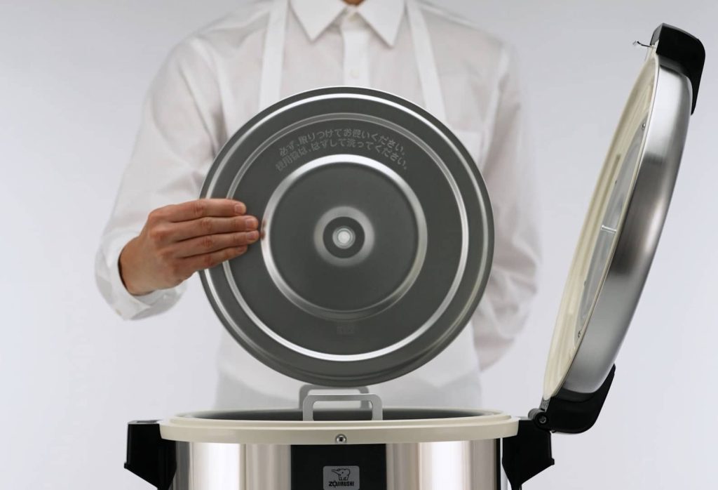 A person wearing a white shirt and apron is holding the inner pan that has been removed