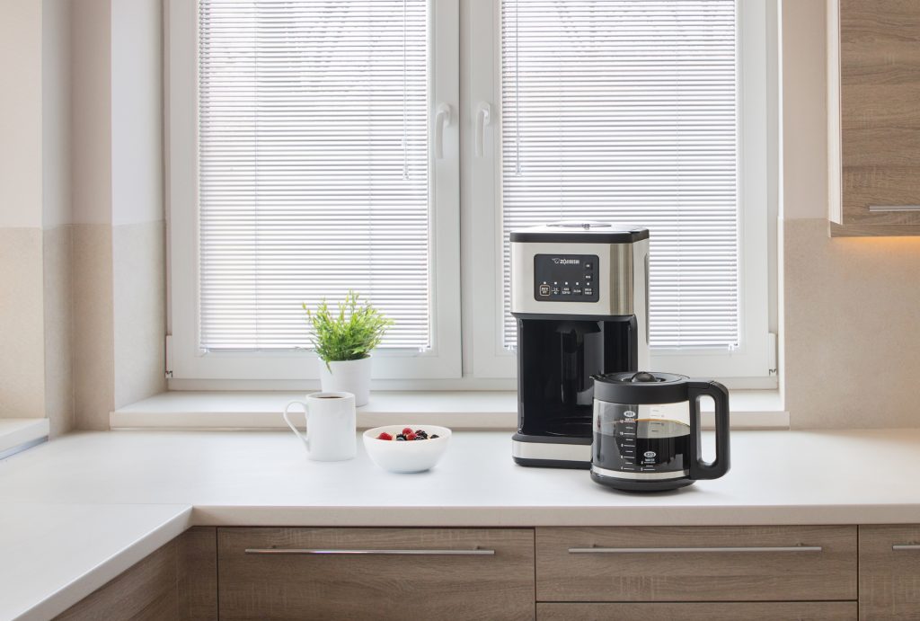 Coffemaker on the white kitchen counter top next to white bowl and white mug