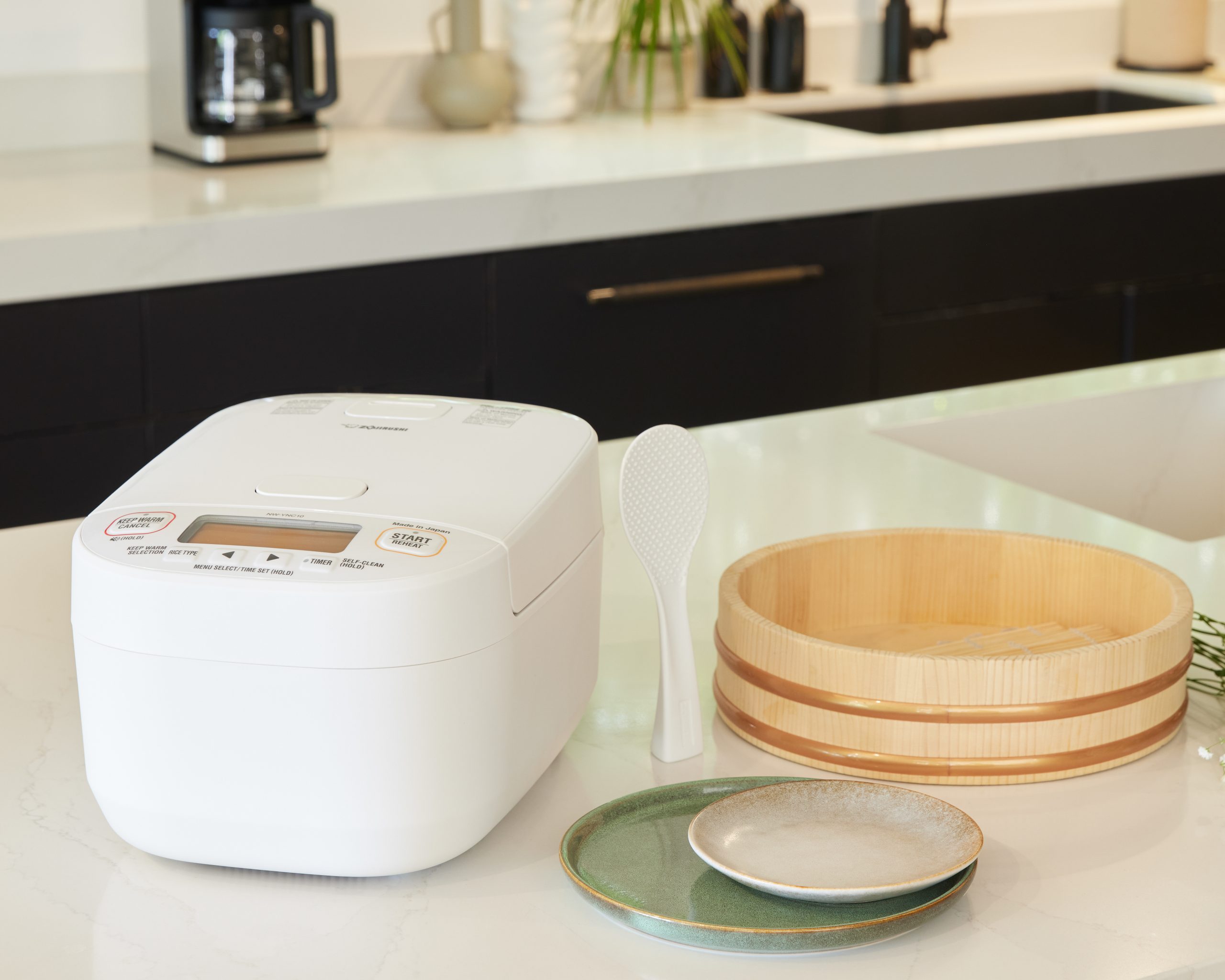 White rice cooker in the kitchen next to plates and a bowl