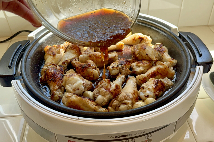 pouring sauce onto Korean style braised chicken in electric skillet
