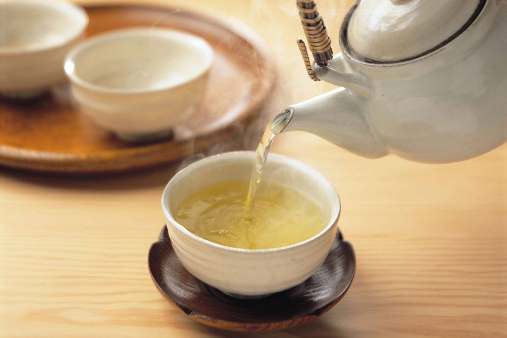 Pouring green tea into a cup from a tea pot