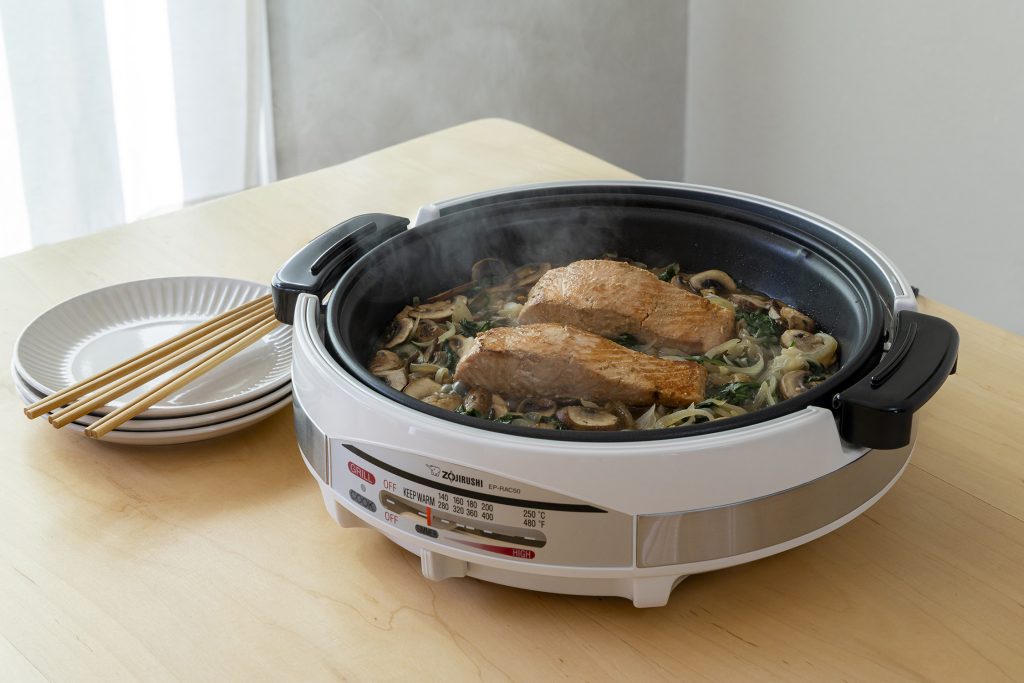 Salmon and veggies being cooked in an electric skillet