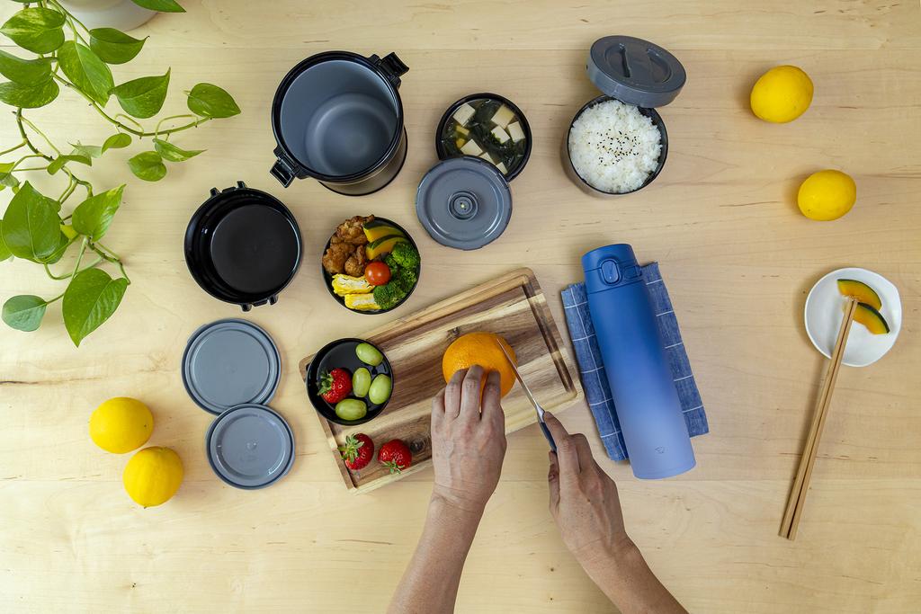 Cutting orange next to opened Mr. Bento and a blue bottle