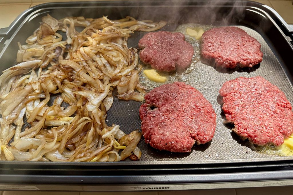 onions and burger patties cooking on griddle