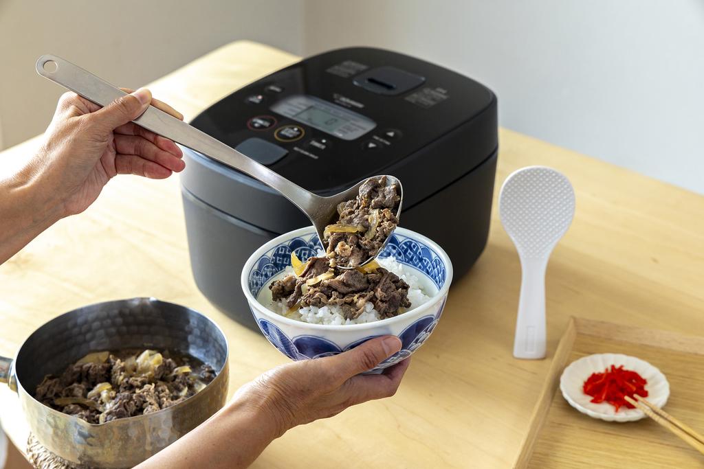 Pouring beef on the rice bowl, black rice cooker in the back