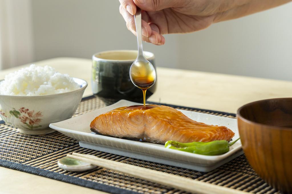 Pouring teriyaki sauce on the salmon with spoon