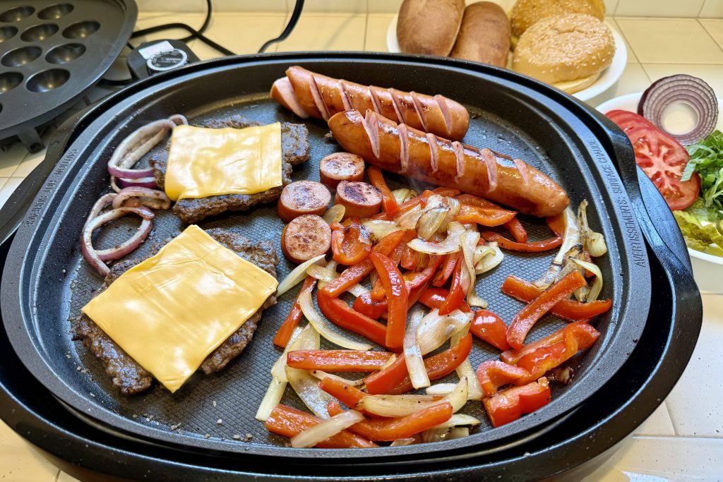 on the griddle: smash burger patties with melting cheese, Polish sausages, frying onions and red peppers