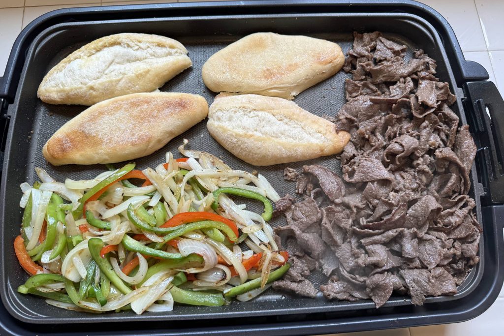 Frying rib-eye beef slices and onions, peppers on electric griddle