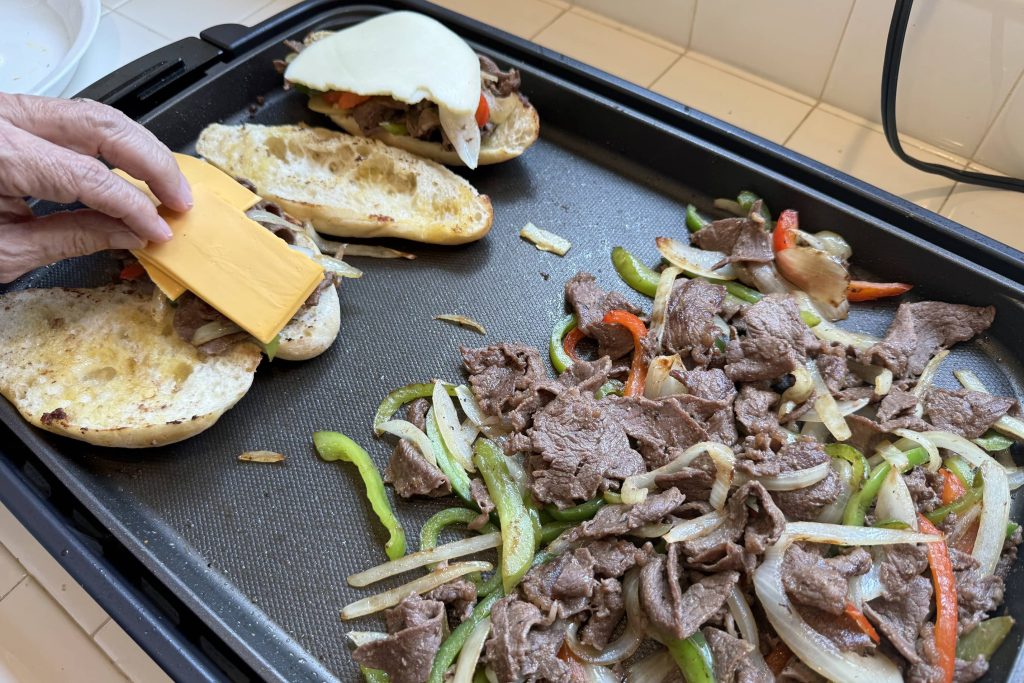 Laying American cheese on Philly cheesesteak sandwich