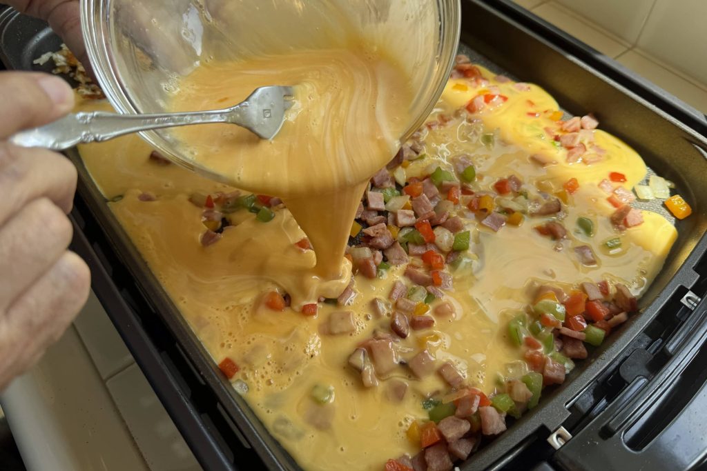 Pouring eggs into electric griddle with Denver ingredients