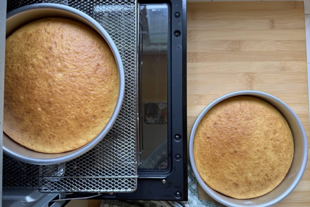 Top view of two yellow cakes in pans next to toaster oven