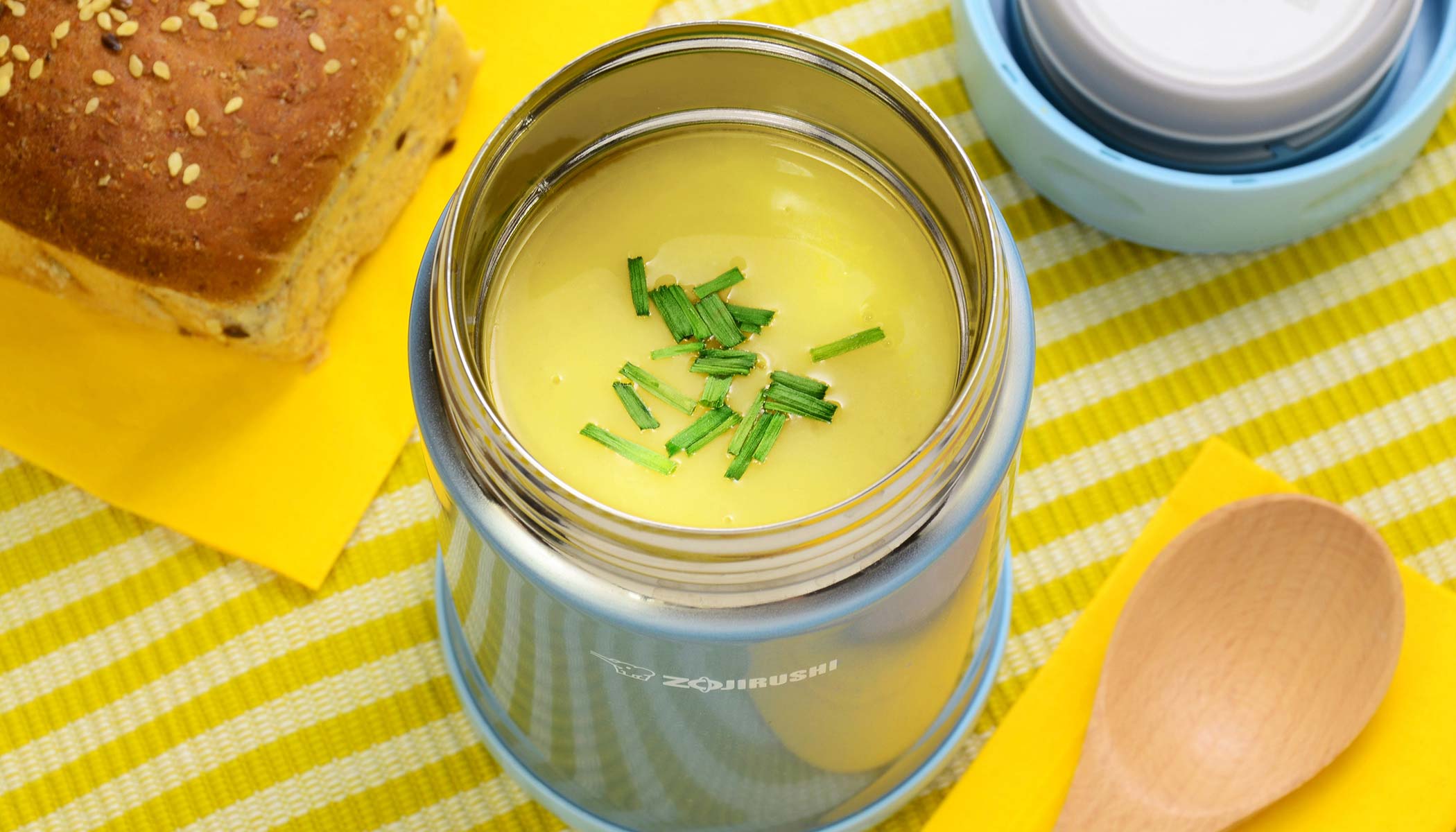 Creamy potato soup served in a blue insulated food jar topped with chives and served with a side of bread